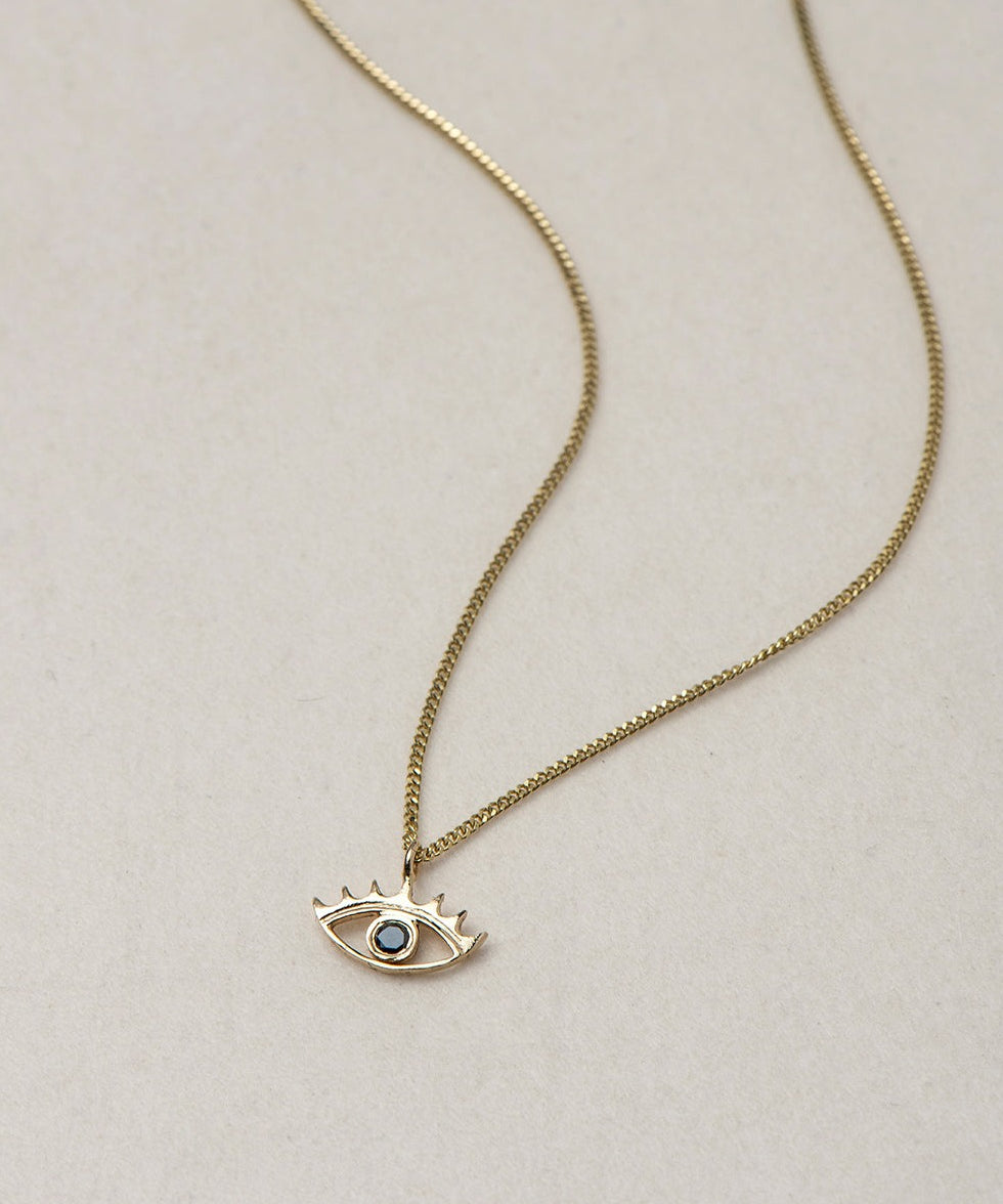 MINI EYE NECKLACE
English

A miniature eye necklace handcrafted in 14K solid gold and suspended from a delicate curb chain. Small in scale yet rich in meaning, it is a quiet symbolic object that balances sculptural simplicity with a sense of protection and inner awareness.

The symbolism of the eye has existed for thousands of years and has always been associated with consciousness and perception. The Evil Eye is worn for protection, the All-Seeing Eye represents divine providence, and the Third Eye symboli