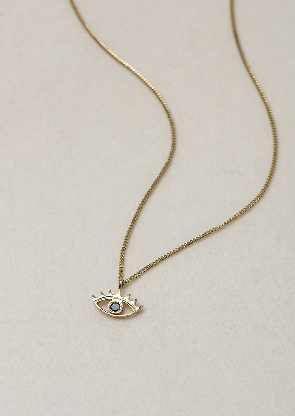 MINI EYE NECKLACE
English

A miniature eye necklace handcrafted in 14K solid gold and suspended from a delicate curb chain. Small in scale yet rich in meaning, it is a quiet symbolic object that balances sculptural simplicity with a sense of protection and inner awareness.

The symbolism of the eye has existed for thousands of years and has always been associated with consciousness and perception. The Evil Eye is worn for protection, the All-Seeing Eye represents divine providence, and the Third Eye symboli