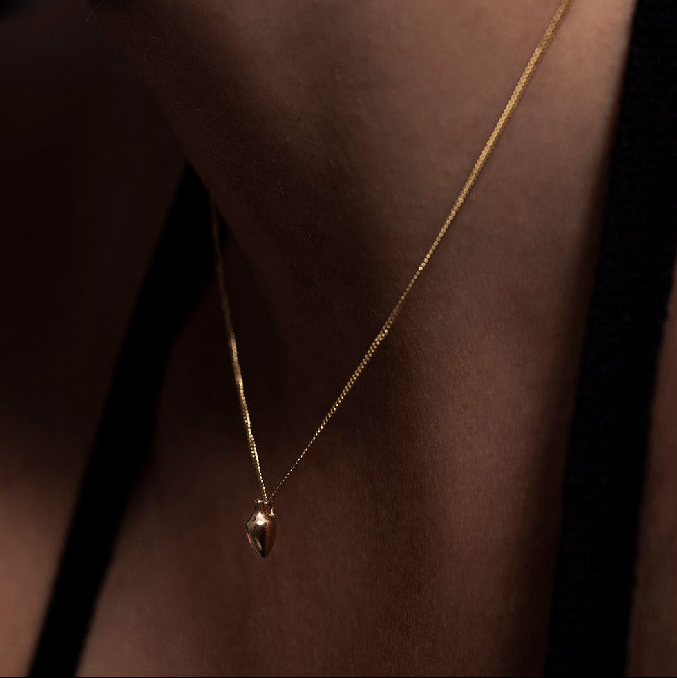 MINI VASE NECKLACE

A miniature vessel necklace handcrafted in 14K solid gold and suspended from a delicate curb chain. Small in scale yet rich in symbolism, it is a sculptural object that balances softness, femininity, and quiet presence.

Throughout history, the vessel has been a feminine, mystical, and ceremonial symbol. In biblical tradition, a vessel represents a person chosen to carry purpose and meaning. At its essence, the vessel symbolizes the human body—particularly the female body that ho