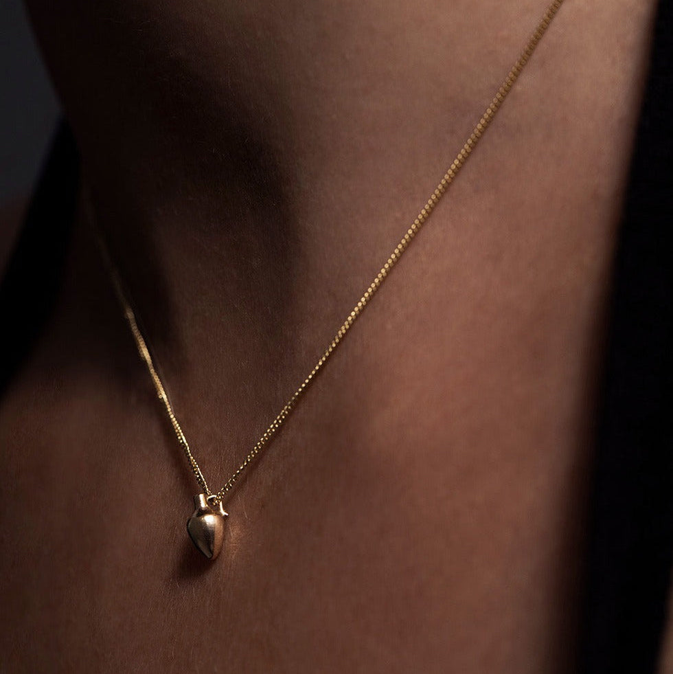 MINI VASE NECKLACE
English

A miniature vessel necklace handcrafted in 14K solid gold and suspended from a delicate curb chain. Small in scale yet rich in symbolism, it is a sculptural object that balances softness, femininity, and quiet presence.

Throughout history, the vessel has been a feminine, mystical, and ceremonial symbol. In biblical tradition, a vessel represents a person chosen to carry purpose and meaning. At its essence, the vessel symbolizes the human body—particularly the female body that ho