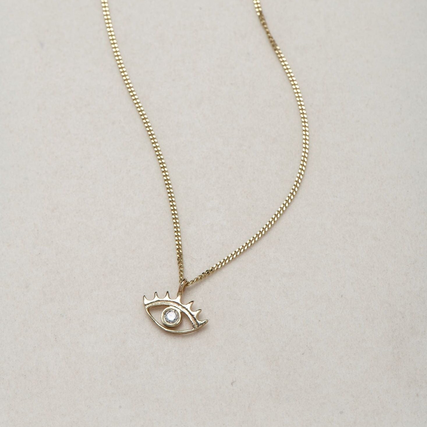 MINI EYE NECKLACE
English

A miniature eye necklace handcrafted in 14K solid gold and suspended from a delicate curb chain. Small in scale yet rich in meaning, it is a quiet symbolic object that balances sculptural simplicity with a sense of protection and inner awareness.

The symbolism of the eye has existed for thousands of years and has always been associated with consciousness and perception. The Evil Eye is worn for protection, the All-Seeing Eye represents divine providence, and the Third Eye symboli