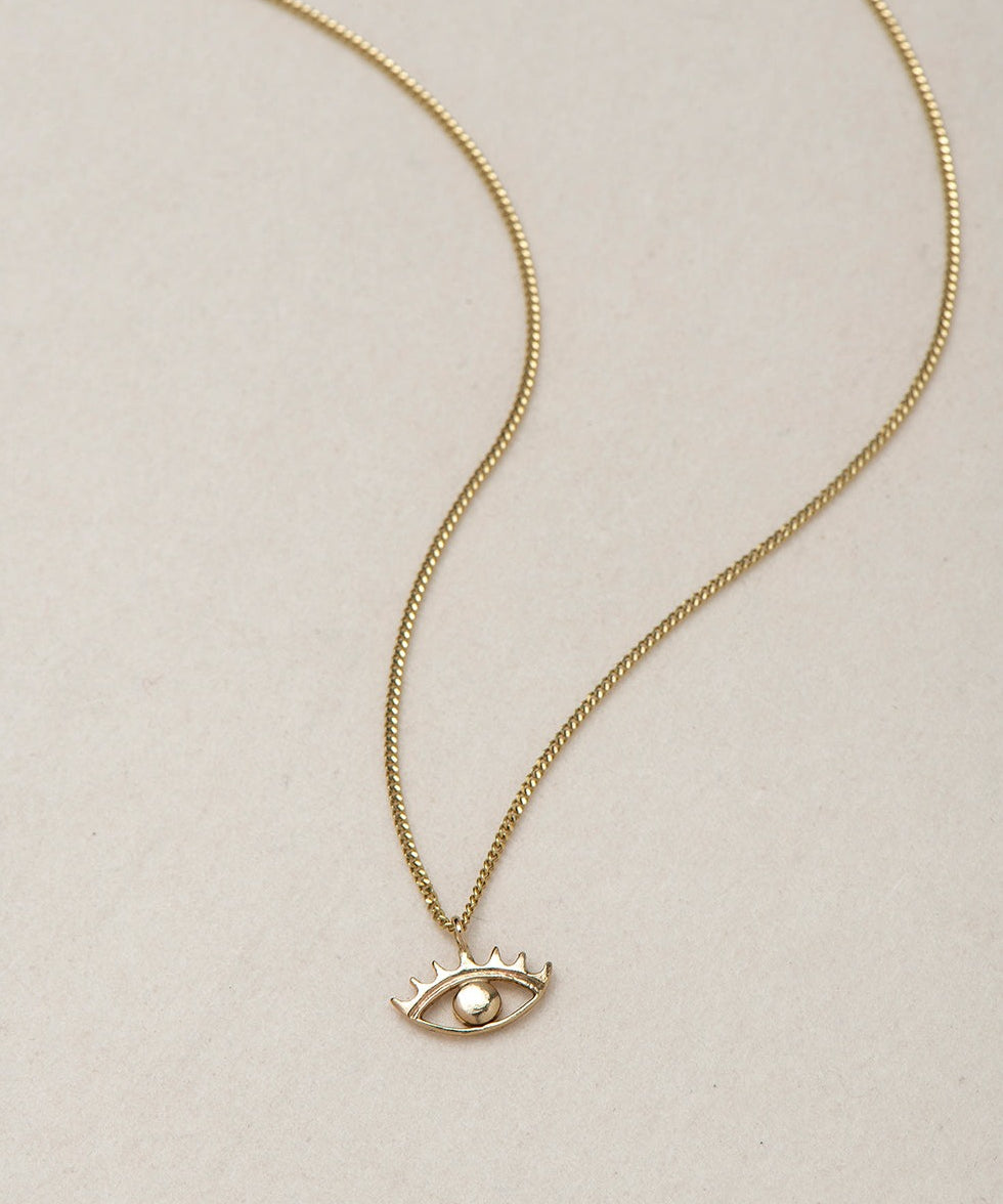 MINI EYE NECKLACE
English

A miniature eye necklace handcrafted in 14K solid gold and suspended from a delicate curb chain. Small in scale yet rich in meaning, it is a quiet symbolic object that balances sculptural simplicity with a sense of protection and inner awareness.

The symbolism of the eye has existed for thousands of years and has always been associated with consciousness and perception. The Evil Eye is worn for protection, the All-Seeing Eye represents divine providence, and the Third Eye symboli