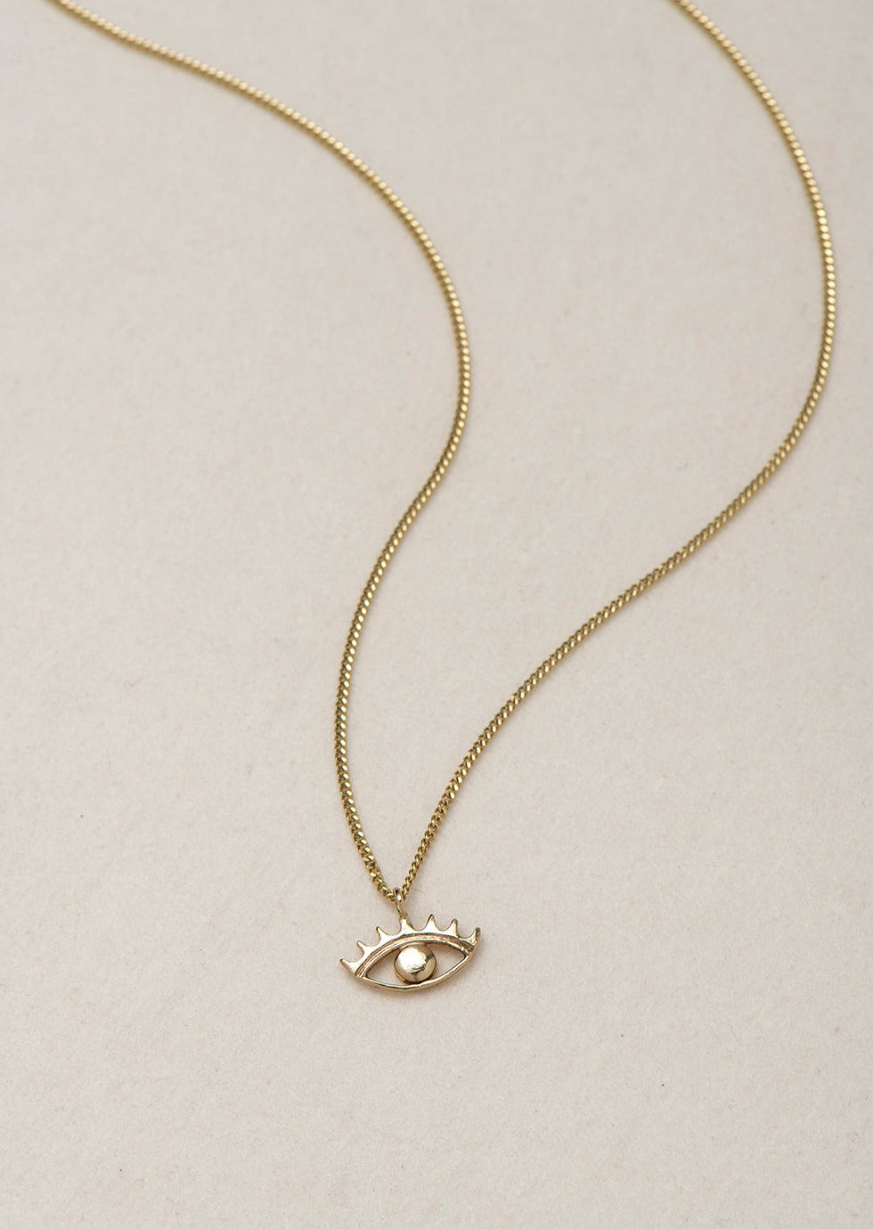 MINI EYE NECKLACE
English

A miniature eye necklace handcrafted in 14K solid gold and suspended from a delicate curb chain. Small in scale yet rich in meaning, it is a quiet symbolic object that balances sculptural simplicity with a sense of protection and inner awareness.

The symbolism of the eye has existed for thousands of years and has always been associated with consciousness and perception. The Evil Eye is worn for protection, the All-Seeing Eye represents divine providence, and the Third Eye symboli