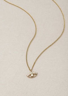 MINI EYE NECKLACE
English

A miniature eye necklace handcrafted in 14K solid gold and suspended from a delicate curb chain. Small in scale yet rich in meaning, it is a quiet symbolic object that balances sculptural simplicity with a sense of protection and inner awareness.

The symbolism of the eye has existed for thousands of years and has always been associated with consciousness and perception. The Evil Eye is worn for protection, the All-Seeing Eye represents divine providence, and the Third Eye symboli